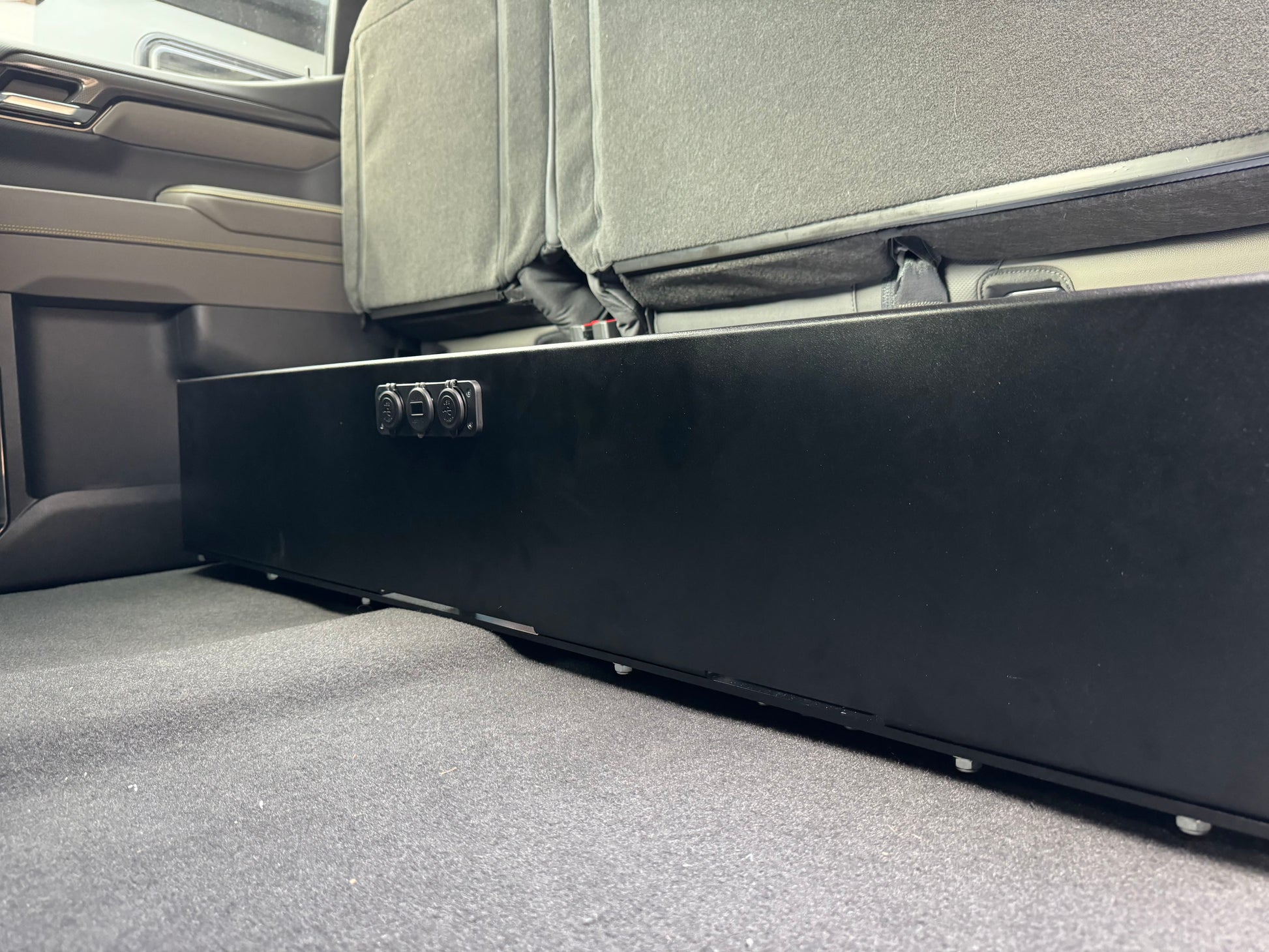 Under seat dual battery storage unit installed in a vehicle, with a black base plate, feet, and straps visible, designed for a Chevrolet Silverado 2019 or newer model.