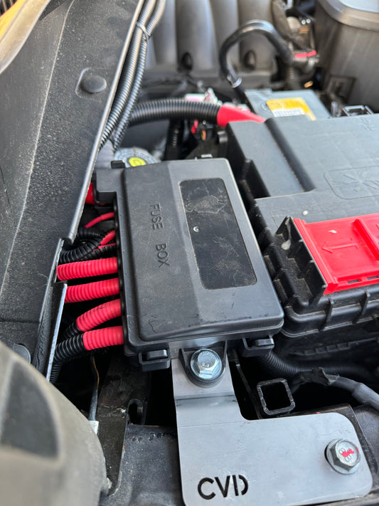 A black 7 way midi fuse holder kit mounted in an engine bay, with red and black wires connected to it for Silverado 1500