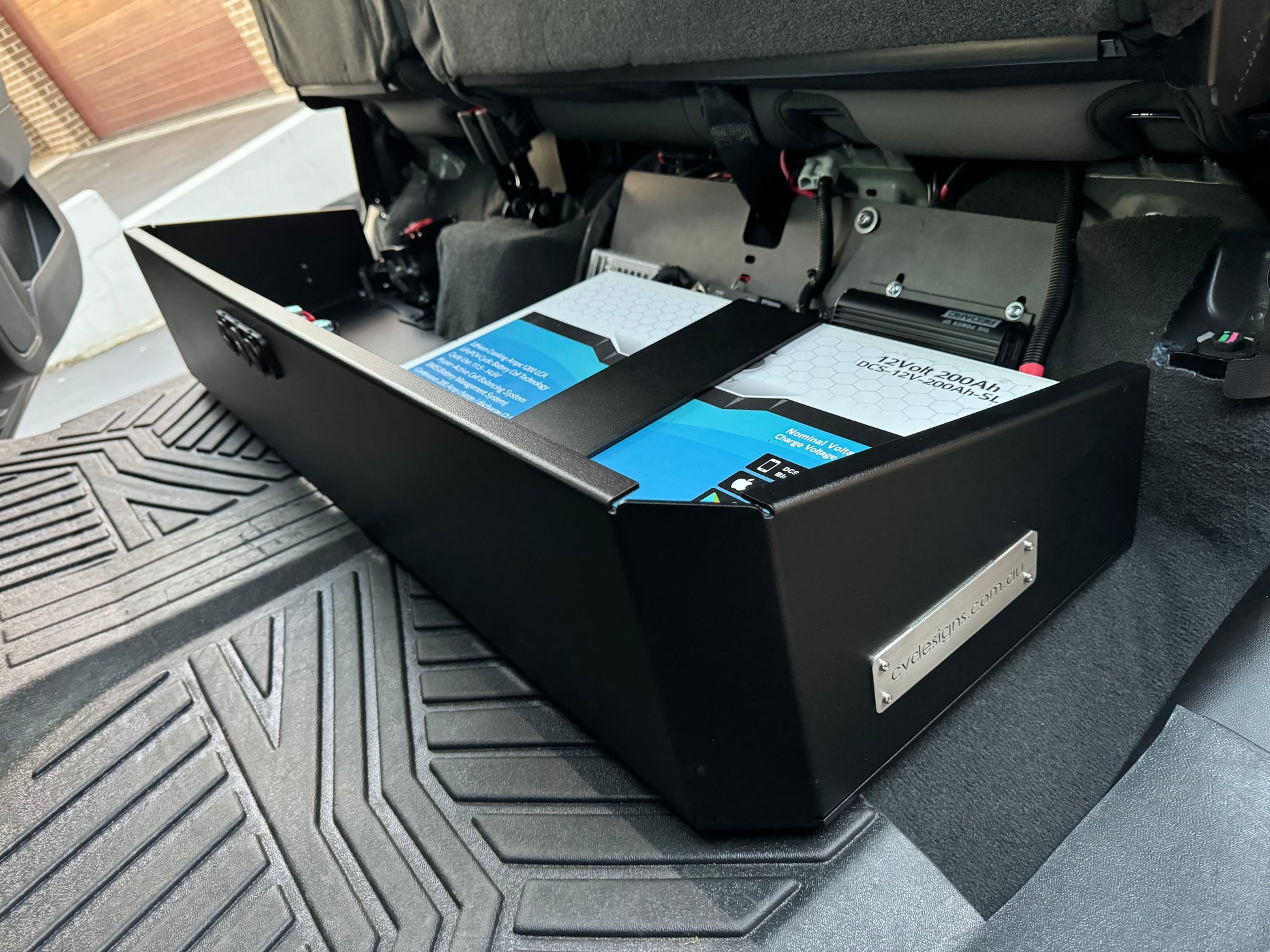 Under seat dual battery storage unit installed in a vehicle, with a black base plate, feet, and straps visible, designed for a Chevrolet Silverado 2019 or newer model.