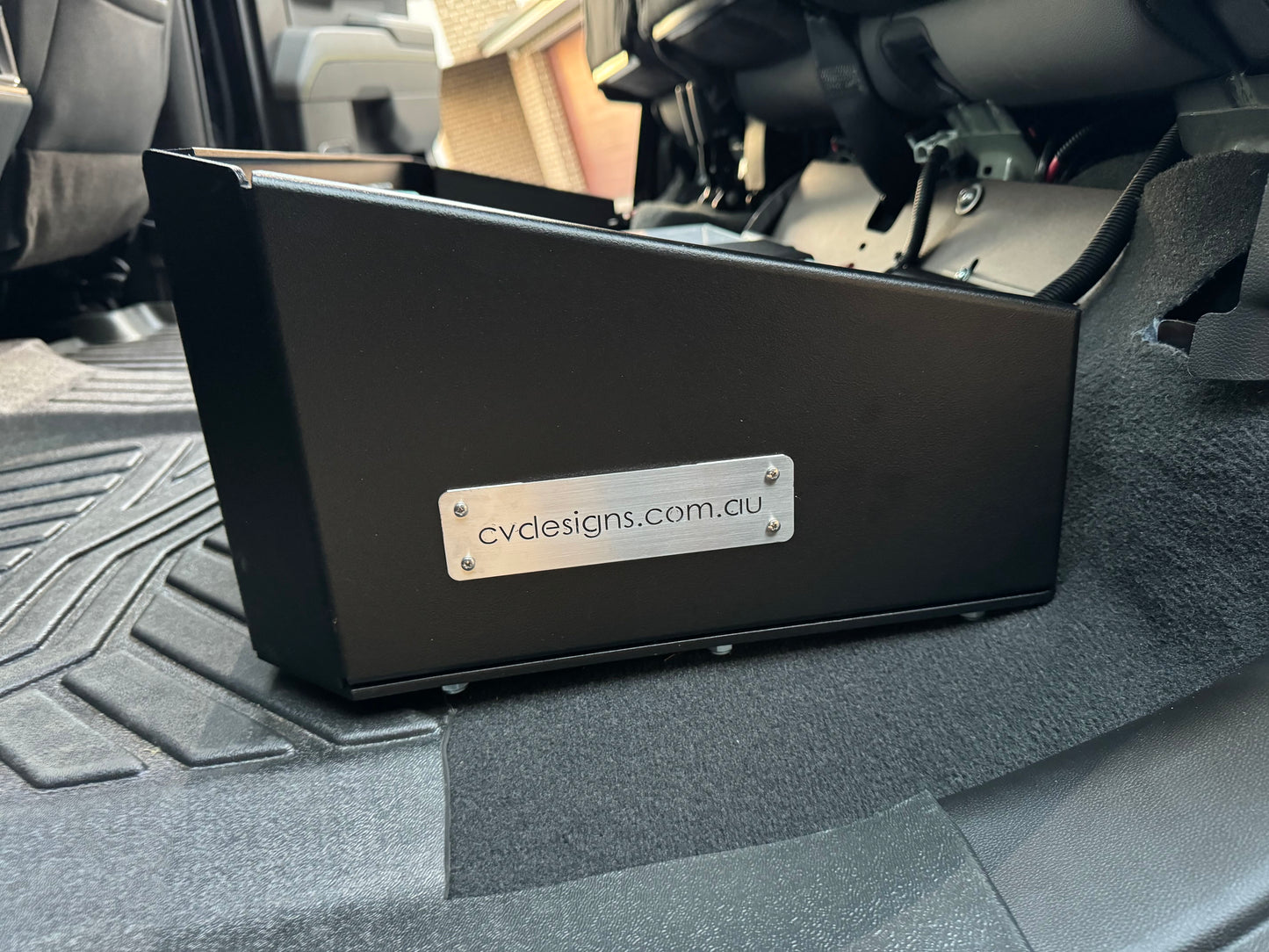 Under seat dual battery storage unit installed in a vehicle, with a black base plate, feet, and straps visible, designed for a Chevrolet Silverado 2019 or newer model.