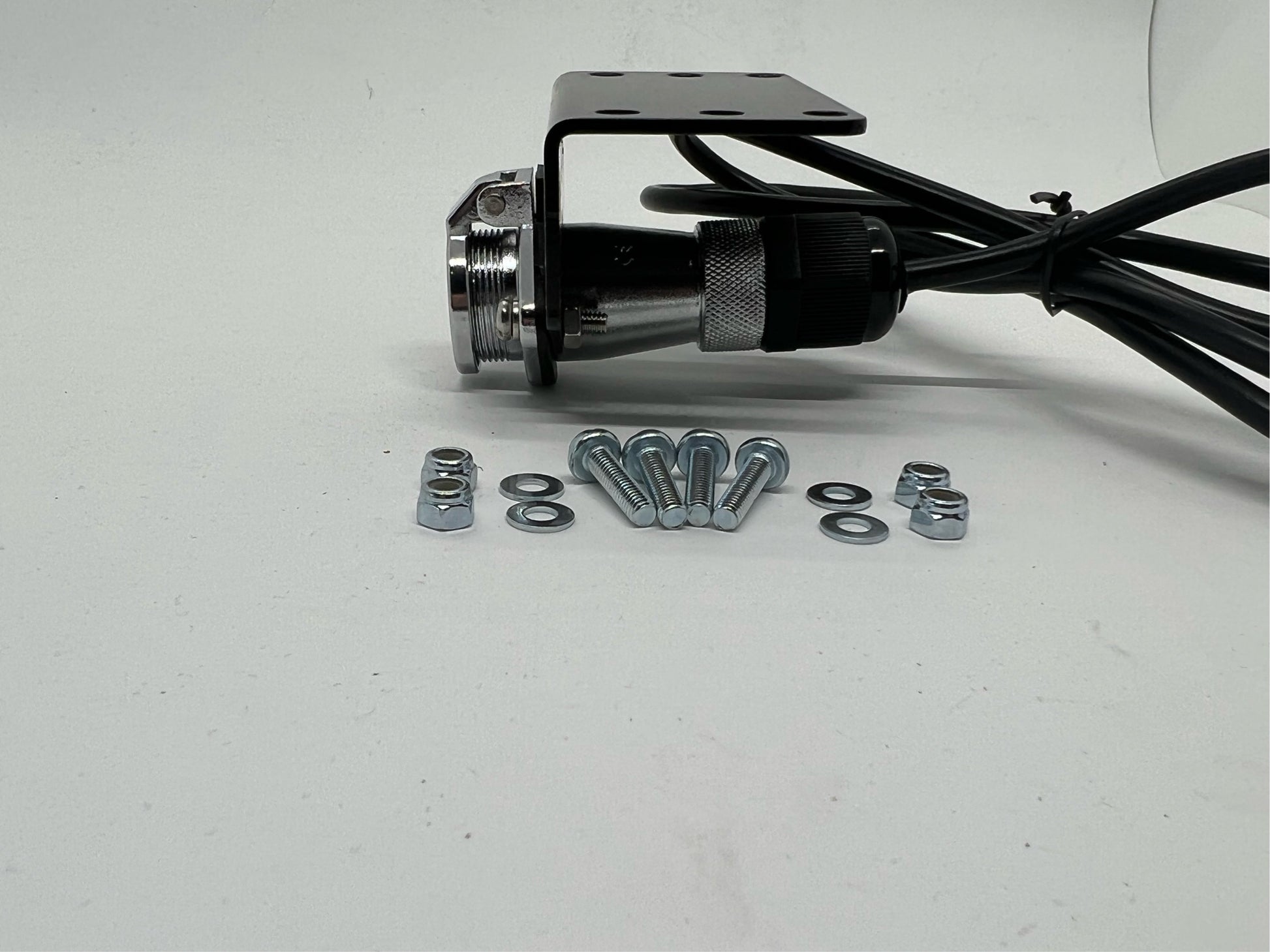 A black steel Wozza Plug Holder Bracket with mounting bolts and a cable, against a white background.