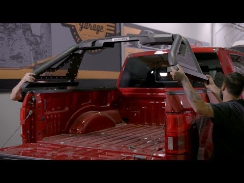 Two people installing a roof rack on a red pickup truck in a garage.