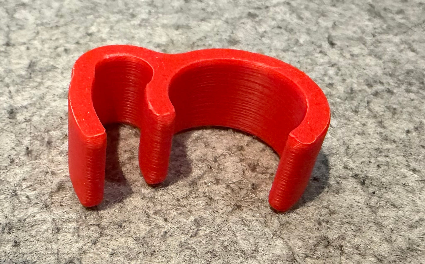 A bright red 3D-printed lawn mower brake lever holder, resting on a textured gray felt surface.
