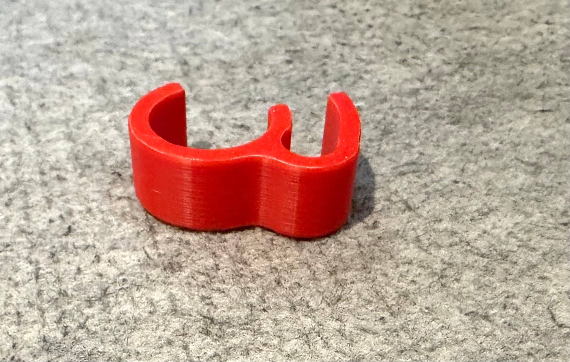 A bright red 3D-printed ring holder or clutch stopper, shown on a textured gray felt surface. Lawn mower Brake Lever Holder