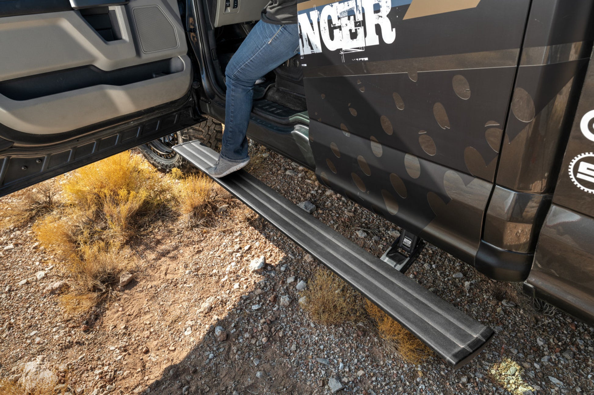 Person using a running board to enter a vehicle on a rugged terrain