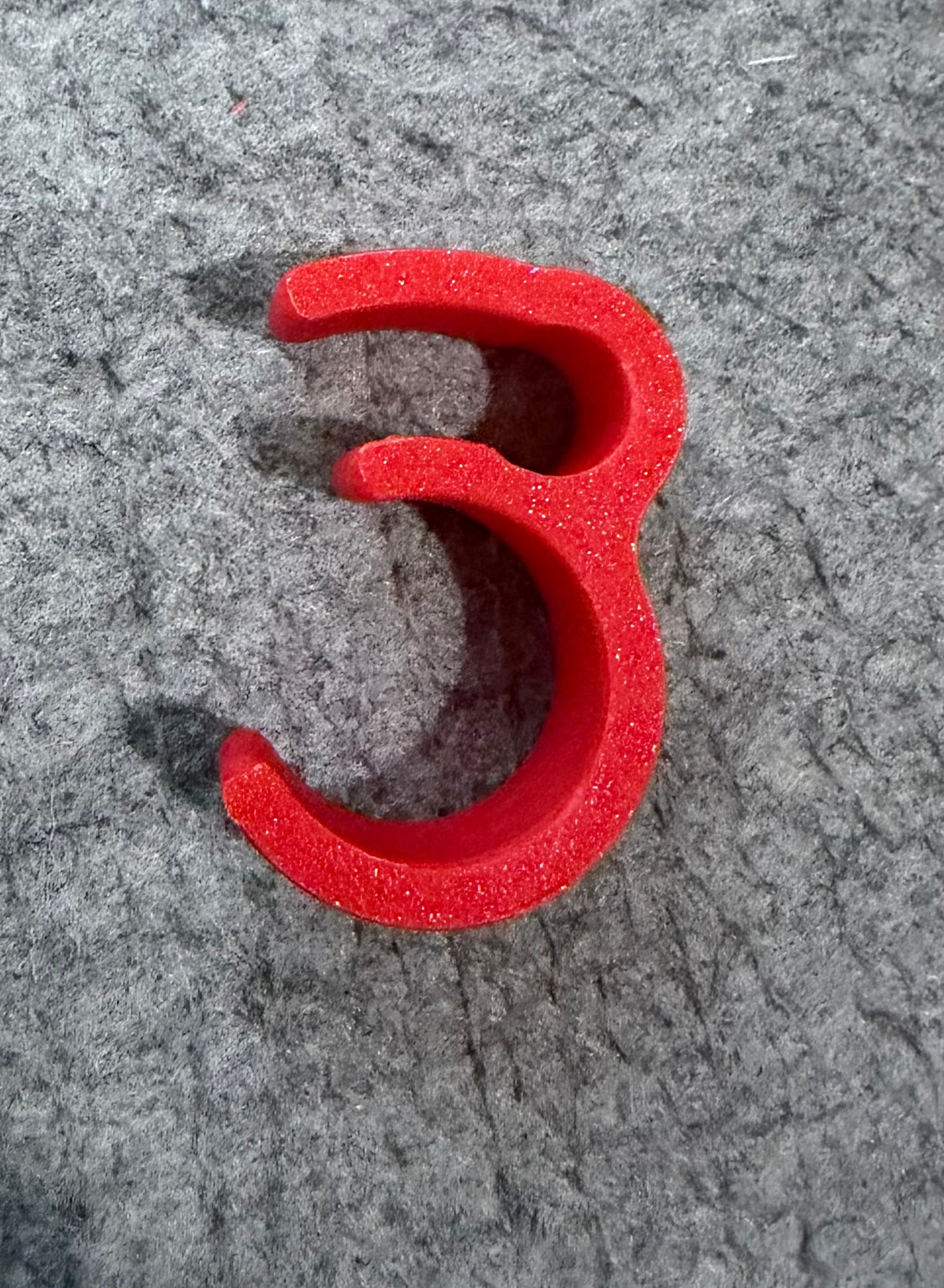 A bright red foam letter '3' cutout, likely a craft or scrapbook embellishment, displayed on a textured gray felt surface.