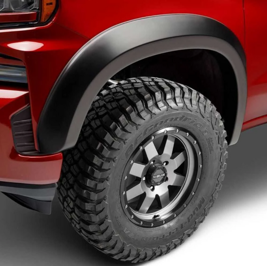 Close-up of a red truck's front wheel area, showing a black Husky Extend A Flare fender, black off-road tire, and a multi-spoke silver and black wheel.